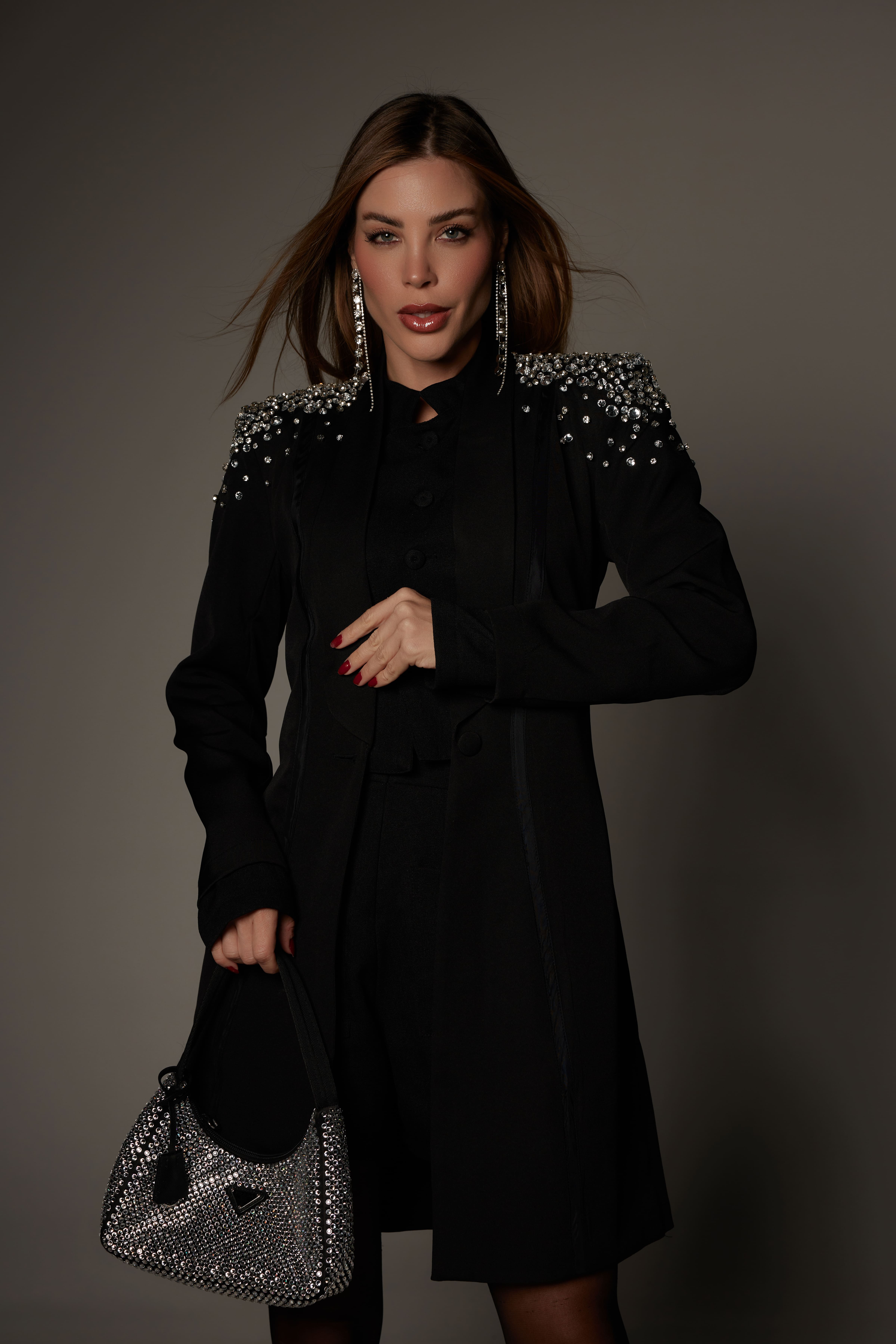 Mulher elegante vestindo Jaleco Black da Virtulle, com bordado de cristais nos ombros, tecido crepe alfaiataria preto, e acabamento de alta qualidade. Ela segura uma bolsa prateada brilhante que complementa o visual sofisticado.